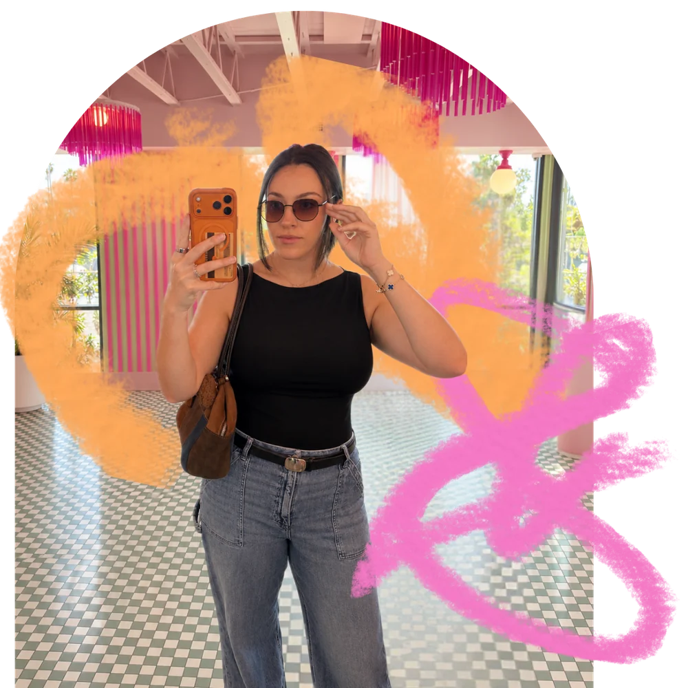 Jaclyn taking a mirror selfie in sunglasses in a bright pink room, with orange and pink brush scribbles